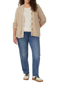 Beige gebreide cardigan met knopen over een gestreepte witte en beige top, gecombineerd met blauwe jeans en crèmekleurige sneakers met zwarte accenten.