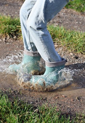 Lichtblauwe rubberlaarzen met grijze gebreide boorden zijn ondergedompeld in modderig water, waardoor er spatten ontstaan, gecombineerd met verweerde blauwe jeans.