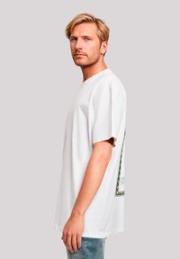 Weißes Baumwoll-T-Shirt, lässige Passform, kurze Ärmel, mit grafischem Design auf der Rückseite in Grün- und Schwarzakzenten, runder Ausschnitt.