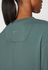 Grön långärmad tröja med ribbad textur, med rundad halsringning och en liten grå Nike-logga på baksidan.