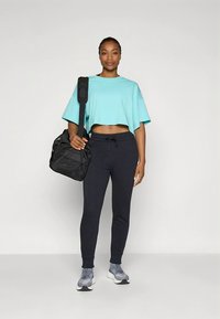 Turquoise cropped t-shirt, black sweatpants, gray sneakers. Large black duffel bag with textured surface. Simple design, suitable for casual wear.