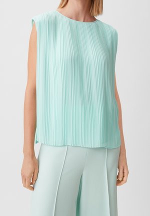 Ærmeløs mintgrøn plisseret bluse kombineret med matchende højttaljede bukser, båret af en stående person foran en ensfarvet baggrund.