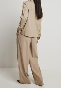 Veste de costume beige ajustée avec une coupe décontractée et des manches longues, associée à un pantalon large, avec une texture lisse et des détails минимaux.