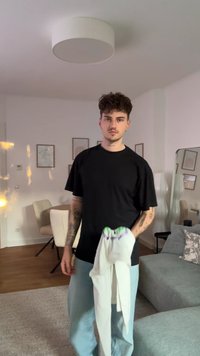 Black oversized t-shirt with short sleeves, worn with light blue jeans. Holding white pants with a green and purple striped waistband.