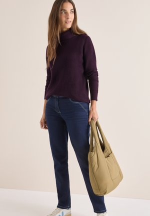 Lila geripptes Sweater mit hohem Kragen, kombiniert mit dunkelblauen geraden Jeans und einer olivgrünen, weichen Tragetasche. Weiße Sneaker mit blauen Akzenten.