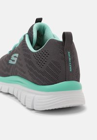 Scarpa da ginnastica grigia con tomaia in rete testurizzata, dettagli verde menta sul collare e sulla suola, e suola esterna bianca imbottita.