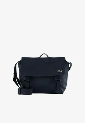 Sac de messager bleu marine avec bandoulière réglable, fermeture à rabat, et petit logo de crocodile vert sur le côté droit avant.