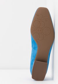 Chaussure en daim bleu avec semelle marron affichant des pièces embossées et le texte "KAISER" et "Peter Kaiser Allemagne depuis 1838" avec la taille 4½.