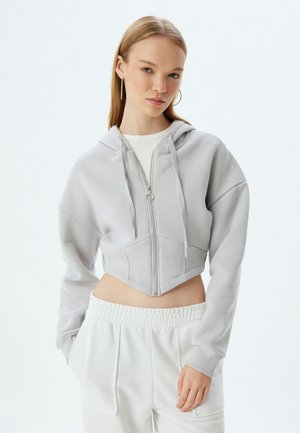 Korte lichtgrijze hoodie met rits, voorzien van een capuchon, lange mouwen en voorzakken. Heeft een gestructureerde stof en een zilveren rits.