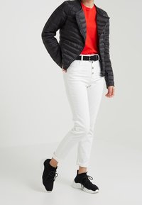 Veste rembourrée noire, t-shirt rouge, jean blanc, ceinture noire et blanche, et baskets noires. Le tissu semble lisse ; les jeans ont une coupe ajustée.