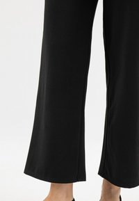 Czarne spodnie z szerokimi nogawkami o gładkiej teksturze, z prostym dołem i długością do kostek. Bez widocznych wzorów ani akcentów.