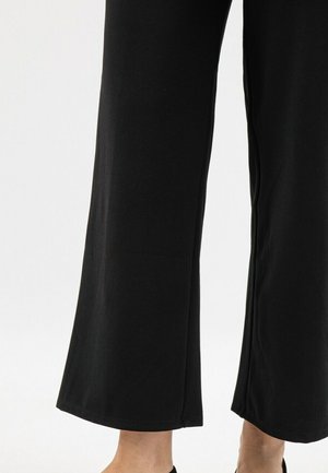 Pantaloni neri a gamba larga con una texture liscia, caratterizzati da un orlo dritto e un taglio alla caviglia. Nessun motivo o dettaglio visibile.
