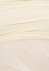 Svijetložuta tkanina koja prikazuje teksturirane, slojevite zavjese. Mekani materijal s suptilnim sjajem, s različitim nijansama u preklapajućim dijelovima.