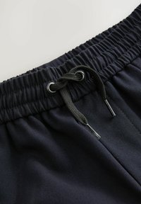 Shorts noirs avec une taille élastique et un cordon de serrage. Le tissu semble lisse avec un léger éclat et est léger. Détail en métal argenté.