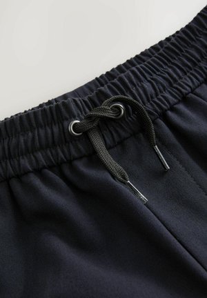 Shorts noirs avec une taille élastique et un cordon de serrage. Le tissu semble lisse avec un léger éclat et est léger. Détail en métal argenté.