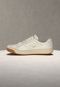 Baskets basses en cuir blanc avec semelle beige, embout perforé, lacets blancs et logo "BALLY" sur le côté et à l'arrière.