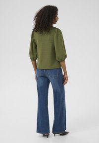 Olivenfarvet tekstureret top med puffede ærmer, parret med højtsiddende blå brede jeans. Sorte spidse hæle fuldender looket.