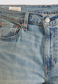 Jean en denim bleu clair avec poche à monnaie visible, fermeture par bouton, passants pour ceinture et étiquette "Levi's Premium" sur la ceinture.