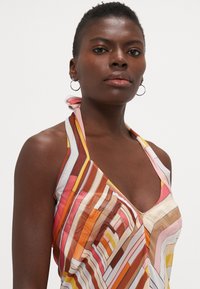 Pestrý šaty s halter výstrihom majú horizontálne pruhy v odtieňoch ružovej, oranžovej, hnedej a žltej farby, vyrobené z ľahkej, štruktúrovanej tkaniny.