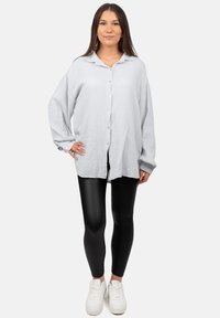 Camicia button-up grigia chiara, texturizzata, con colletto, abbinata a leggings neri e sneaker bianche. La camicia ha una vestibilità comoda e spalle scese.