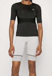 Lyhythihainen musta urheilu paita, jossa on verkkokankaita ja logo, yhdistettynä vaaleanharmaisiin istuviin shortsisiin, joissa on musta raita helman kohdalla.