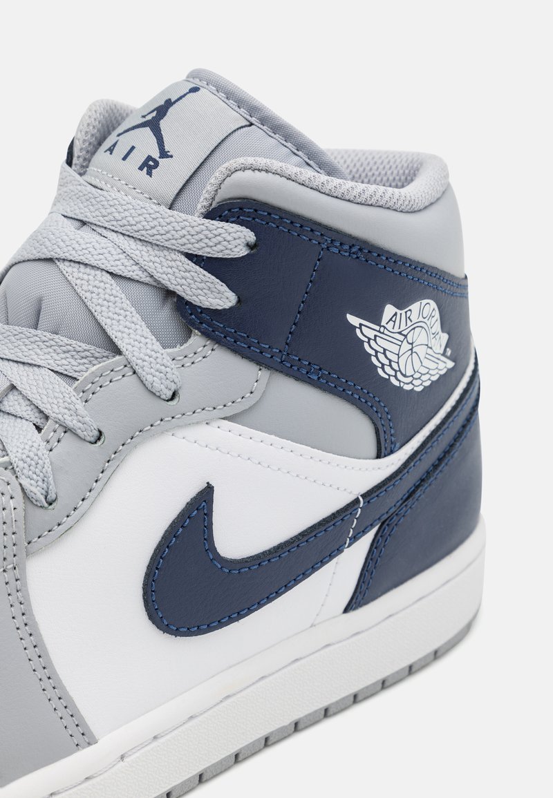 Zapatillas de media caña que presentan una combinación de colores en gris, blanco y azul marino. Fabricadas en cuero y malla, con un prominente logo de Air Jordan y acentos bordados.