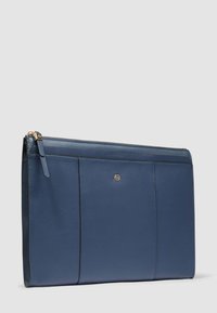 Portafoglio clutch in pelle blu con cerniera, con un piccolo emblem a logo dorato sul davanti, su uno sfondo chiaro e uniforme.