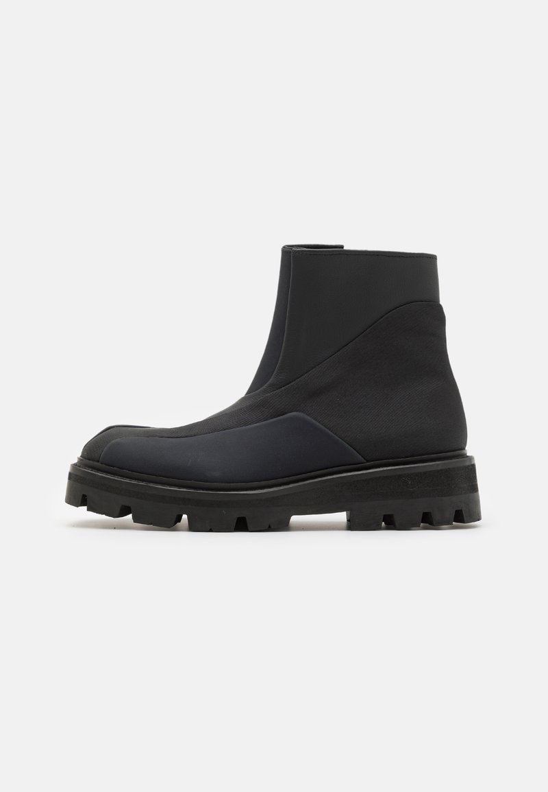 Mustat nilkkurit, joissa on teksturoidusta materiaalista yläosa, kontrastisia matta- ja kiiltopintoja sekä paksu kumipohja, jossa on urat.