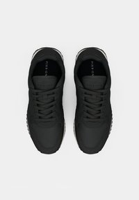 Mustat urheilukengät, joissa on teksturoitu materiaali, pyöreä kärki, pehmustettu kaulus ja litteät nauhat. Kengissä on hienovarainen brändäys kielekkeessä ja pohjassa.