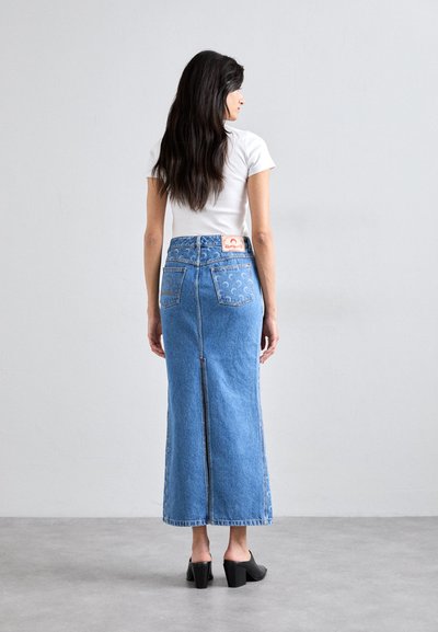 Denim maxi skirt with a fitted waist, back split, and intricate stitching details. Light blue wash with two back pockets and logo patch.