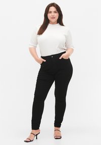 Jeans skinny negros con cintura alta, bolsillos frontales y cierre de un solo botón. Combinados con una camiseta blanca de manga corta acanalada.