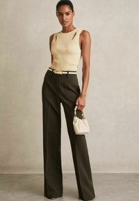 Top beige a costine con dettagli a taglio, abbinato a pantaloni verde scuro a vita alta e una borsa color crema con decorazioni di perline.
