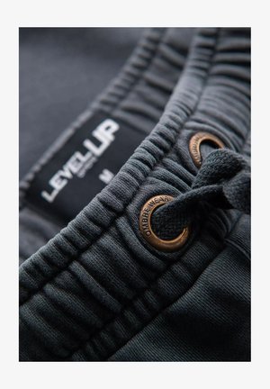 Grijze katoenen shorts hebben een rekbare tailleband met een verstelkoord, verfraaid met bronzen oogjes en een label met de tekst "LEVEL UP."