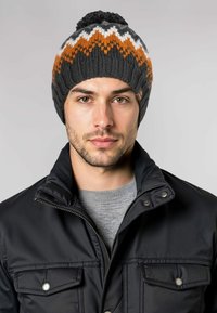 Gebreide beanie met een pompom, met een kleurrijk zigzagpatroon in oranje, wit en zwart. Zachte textuur en warm materiaal.
