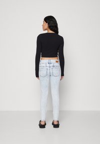 Crni dugi rukavi uski crop top u kombinaciji s svijetlim opranim uskim trapericama. Traperice imaju stražnje džepove i oznaku branda na pojasu.