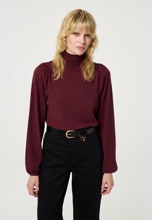 Bordeaux rood longsleeve shirt met een hoge halslijn en pofmouwen, gecombineerd met zwarte high-waisted broek en een zwarte riem met een gouden gesp.