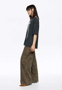 Oversized czarny t-shirt z grafiką w połączeniu z luźnymi, teksturowanymi oliwkowymi spodniami z subtelnym wzorem i zwężanym dołem.