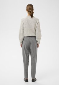 Maglione grigio chiaro a maglia con finitura testurizzata, abbinato a pantaloni grigi con righe sottili a vita alta e scarpe nere senza tacco.