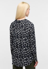 Langærmet bluse med et marineblåt og cremefarvet cirkulært mønster, lavet af en glat stof med en afslappet pasform og en subtil kravedetalje.