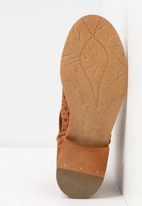 Dessous de chaussure en cuir perforé marron avec un arrière lisse couleur beige clair, présentant des logos gravés et une semelle texturée pour une meilleure adhérence. Taille 37.