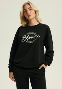 Czarny sweatshirt z nadrukiem z przodu z napisem „Bloonii” i okrągłymi akcentami. Miękka tkanina z ściągaczami przy mankietach i okrągłym dekoltem.