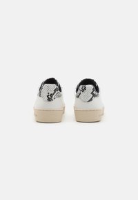 Sneakers bianche con dettagli in stampa pitone nera e bianca sulla punta, caratterizzate da una suola beige e un design minimalista.