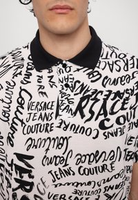 Camisa polo de manga curta com colarinho preto, tecido branco e um ousado padrão de texto abstrato em preto por toda a parte, destacando nomes de marcas.