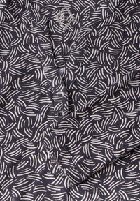 Chemise navy avec un motif abstrait blanc, col en V et deux boutons ronds à l'avant. Tissu doux et texturé.