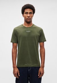 Χακί βαμβακερό μπλουζάκι με στρογγυλή λαιμόκοψη και κοντά μανίκια. Διαθέτει ένα μικρό λογότυπο σε λευκό τυπωμένο στο στήθος. Ομαλή υφή.