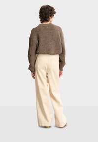 Maglione lavorato a maglia marrone con un design corto, abbinato a pantaloni beige con vestibilità ampia. Tessuto semplice e texture con cuciture visibili.