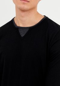 Schwarzes Herren-V-Ausschnitt-T-Shirt, das über einem dunkelgrauen Shirt getragen wird. Weiches Baumwollmaterial mit einer glatten Textur und minimalen Nähdetails.