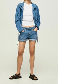 Světle modrá bunda se stahovacími šňůrkami, bílý krátký crop top, ohrnuté džínové kraťasy a černé sandály s pásky. Neformální letní outfit.