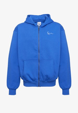 Modrá mikina na zip s kapucí, předními kapsami, žebrovanými manžetami a lemem, kapucí a malým bílým podpisovým logem na levé straně hrudi.