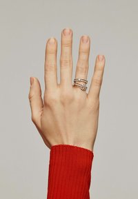 Tres anillos de plata apilados en una mano. Los anillos presentan diversas texturas y patrones, con uno de ellos decorado con pequeñas piedras.